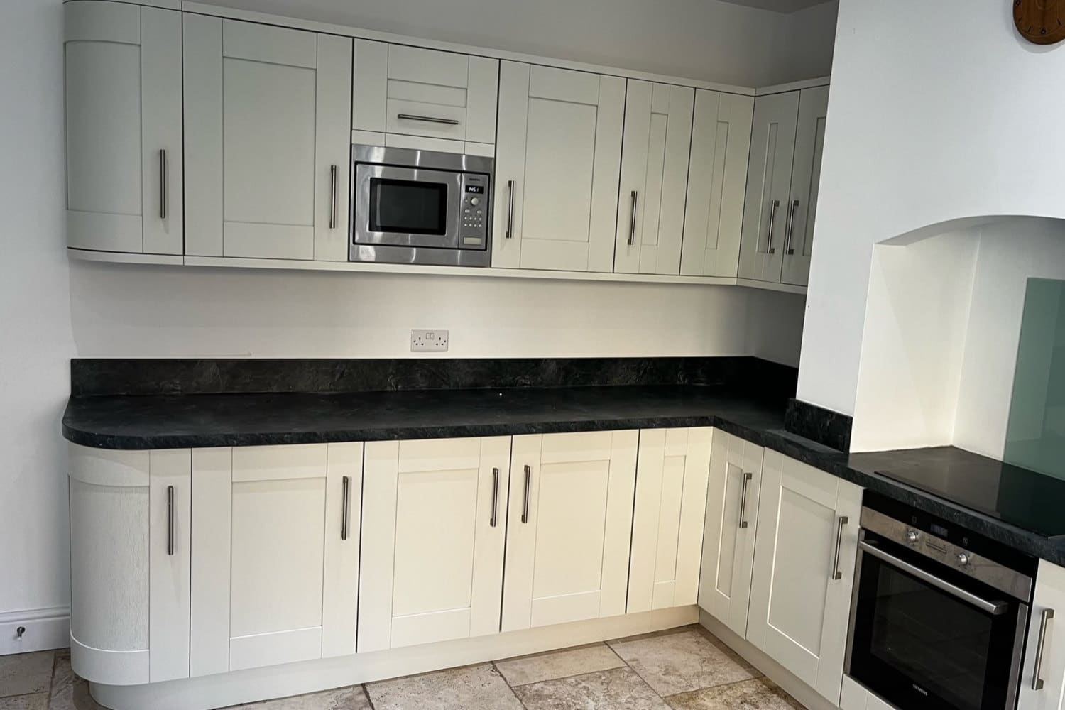 A shaker kitchen resprayed in a soft cream, with curved end units and a dark worktop
